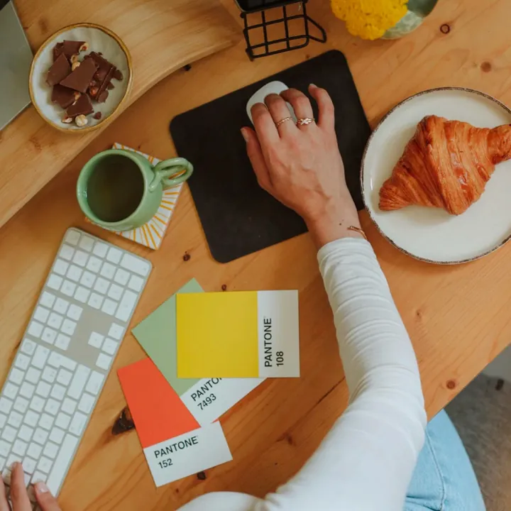 Le bureau du studio : clavier, nuancier Pantone, café et croissant