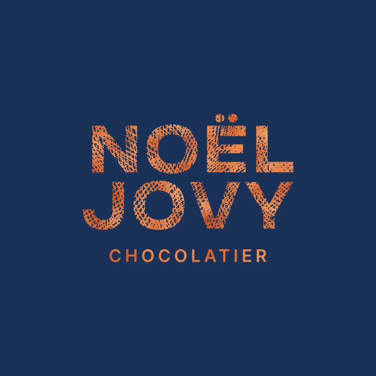 Le logo Noël Jovy empilé, en dorure cuivre sur le bleu marine de la maison