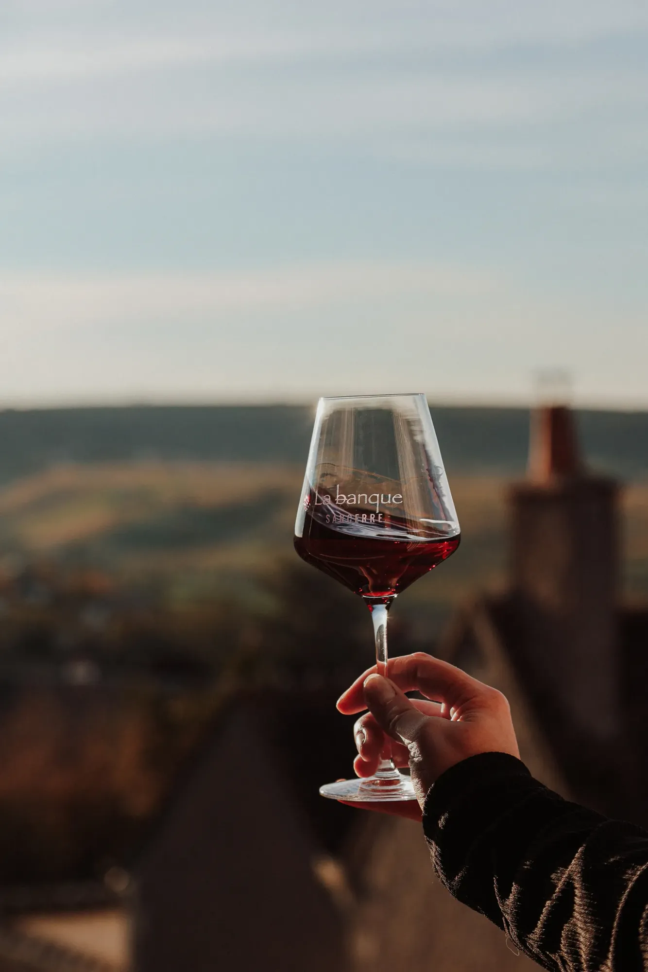 Un verre de vin rouge gravé au nom de La Banque, levé face aux collines de Sancerre