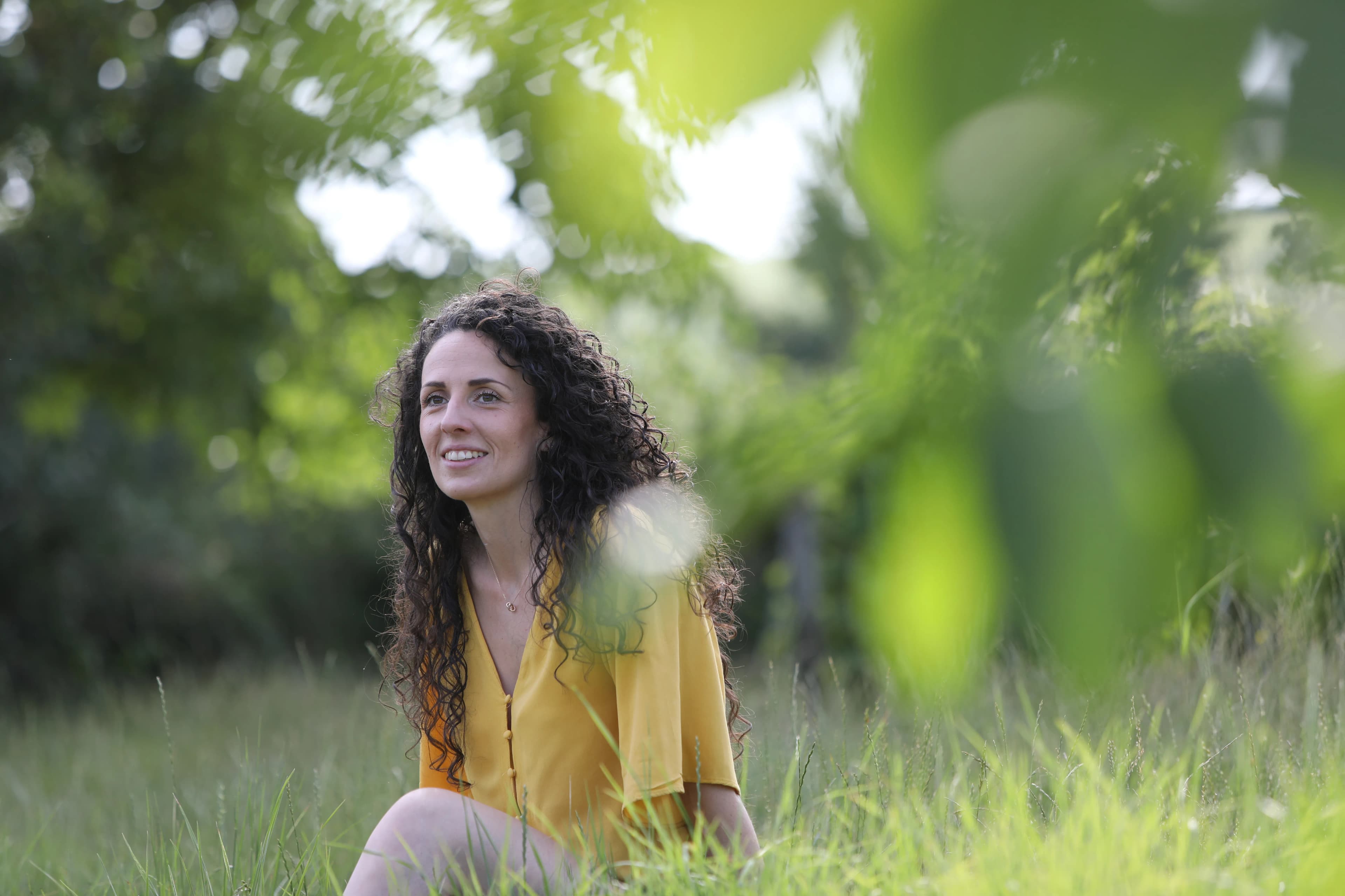 Clémence Piquard assise dans l'herbe, en robe jaune, entourée de verdure