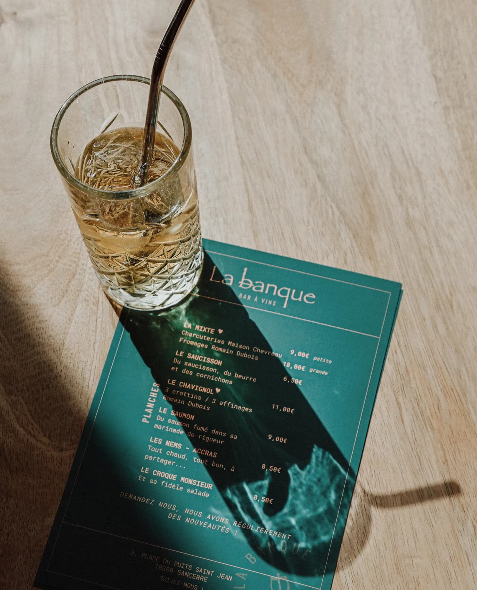 La carte des planches de La Banque sur une table en bois, un cocktail posé dessus