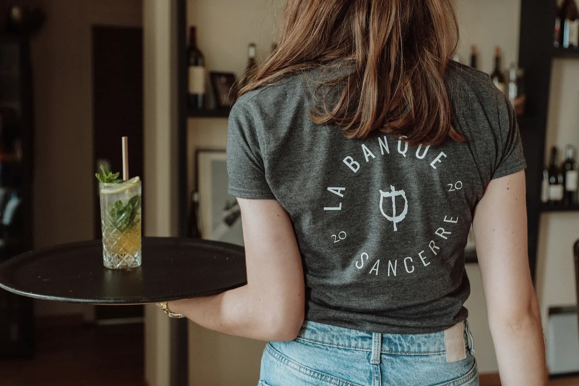 Au dos d'un tee-shirt de La Banque, le B barré pivoté devenu verre à pied